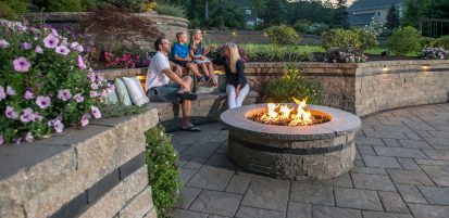 Unilock Outdoor Fire Pit with Family sitting on surrounding Retaining Wall
