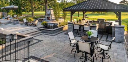 Unilock Outdoor Entertainment Space with Fireplace and Waterfall Features and Kitchen