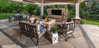 Family Sitting on Patio Around Outdoor Fire Pit and TV Wall