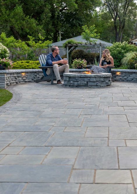 People Sitting by Fire Pit with Retaining Wall with Lights Dividing Patio and Grass