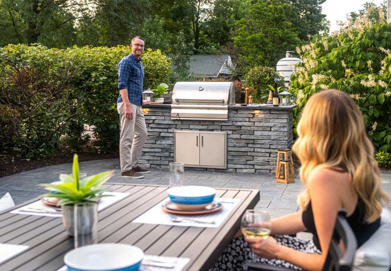 Person Cooking on Kitchen Island Grill and Person Sitting on Patio Dining Table