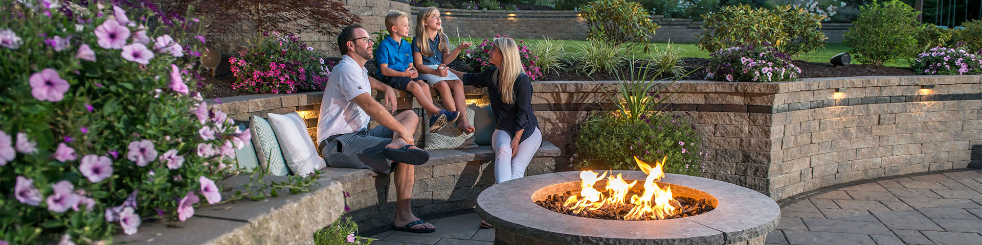 Family sitting on Retaining Wall around Unilock Outdoor Fire Pit 