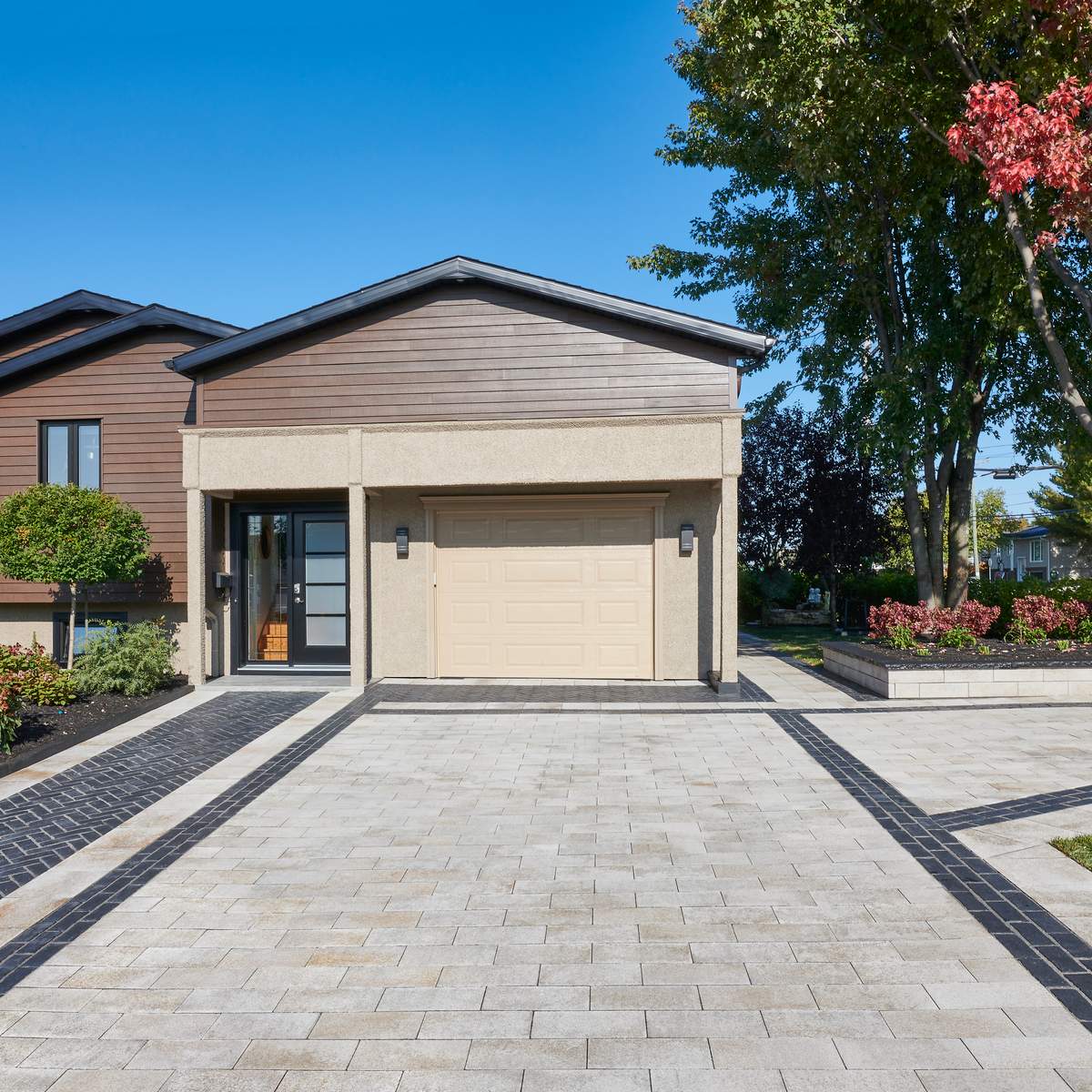 Beige and black Unilock pavers create an intricate pattern leading toward home and garage