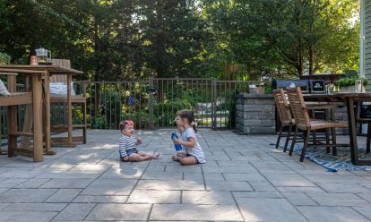 Two children sitting on pavers in their backyard patio.