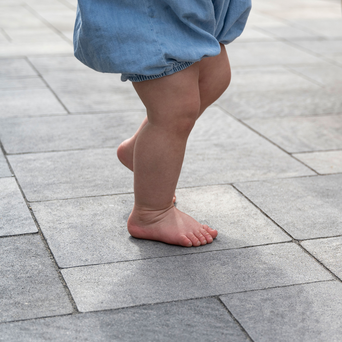 A baby's feet standing on a walkway made of driveway pavers.