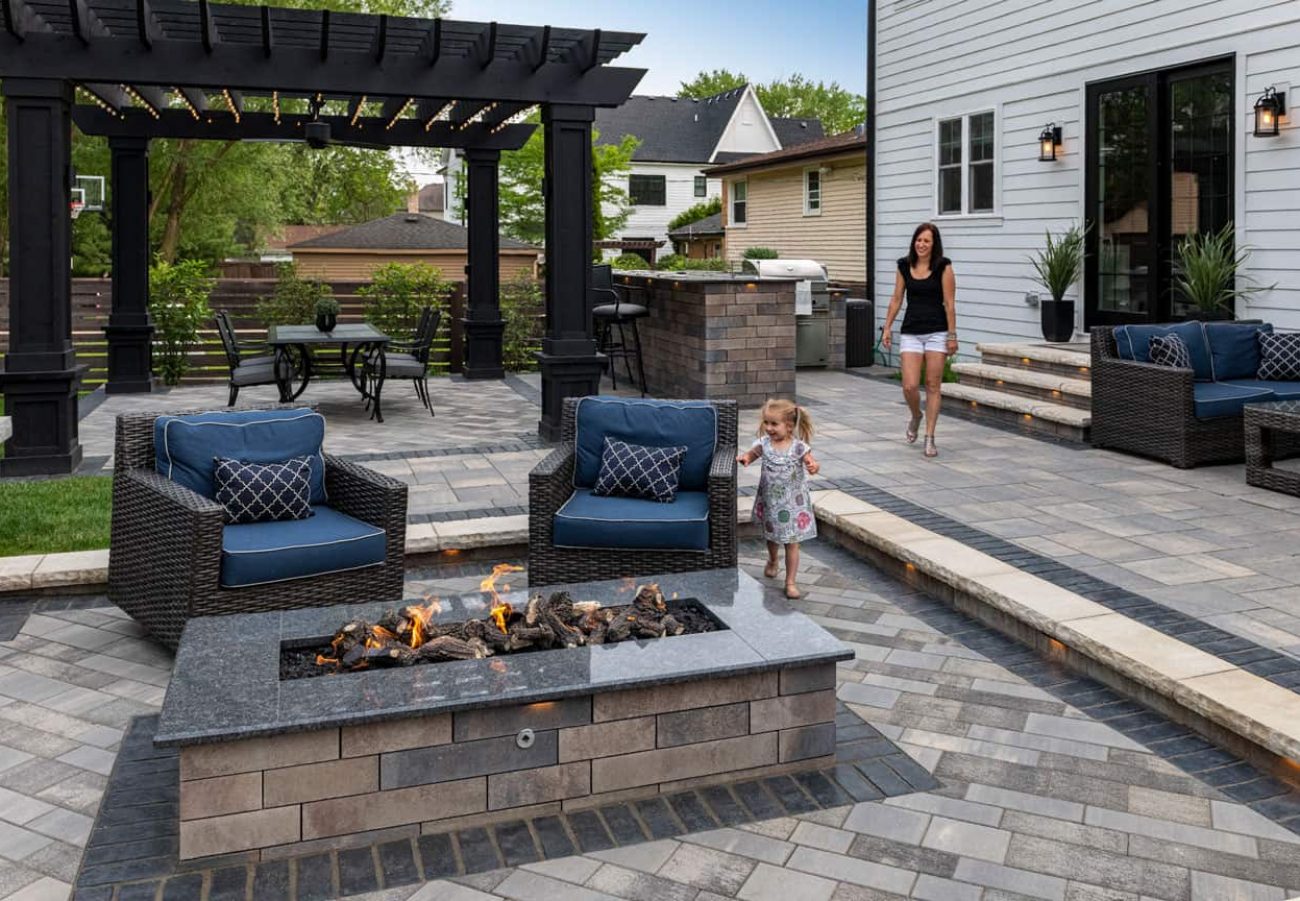 Young Child Walking towards lowered Patio with Fire Feature and Women on Upper Patio with Outdoor Kitchen