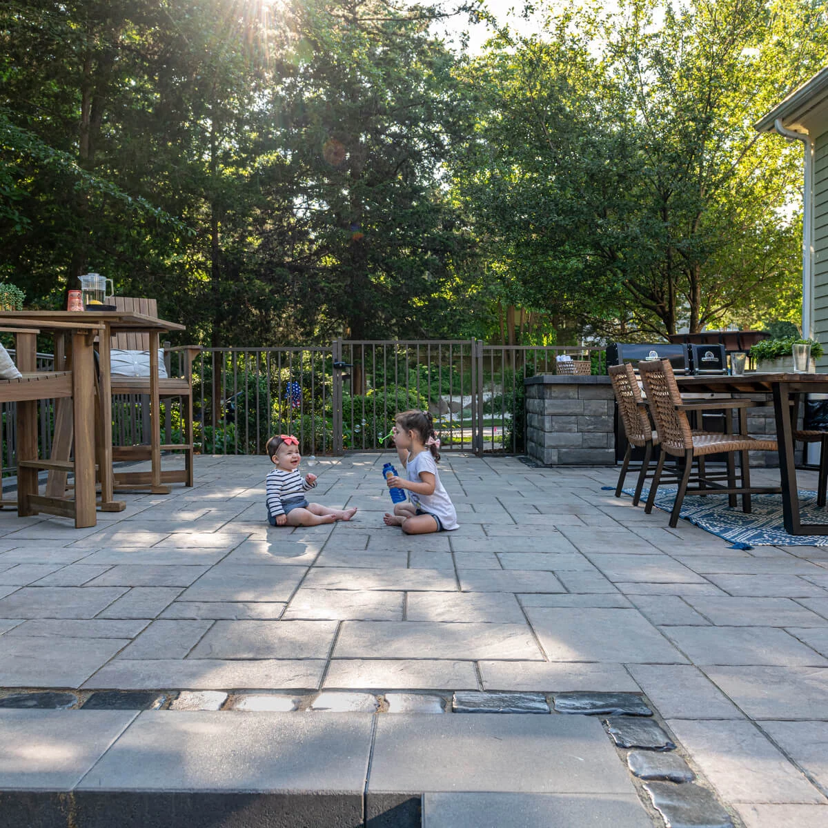 Two children sitting on pavers in their backyard patio.