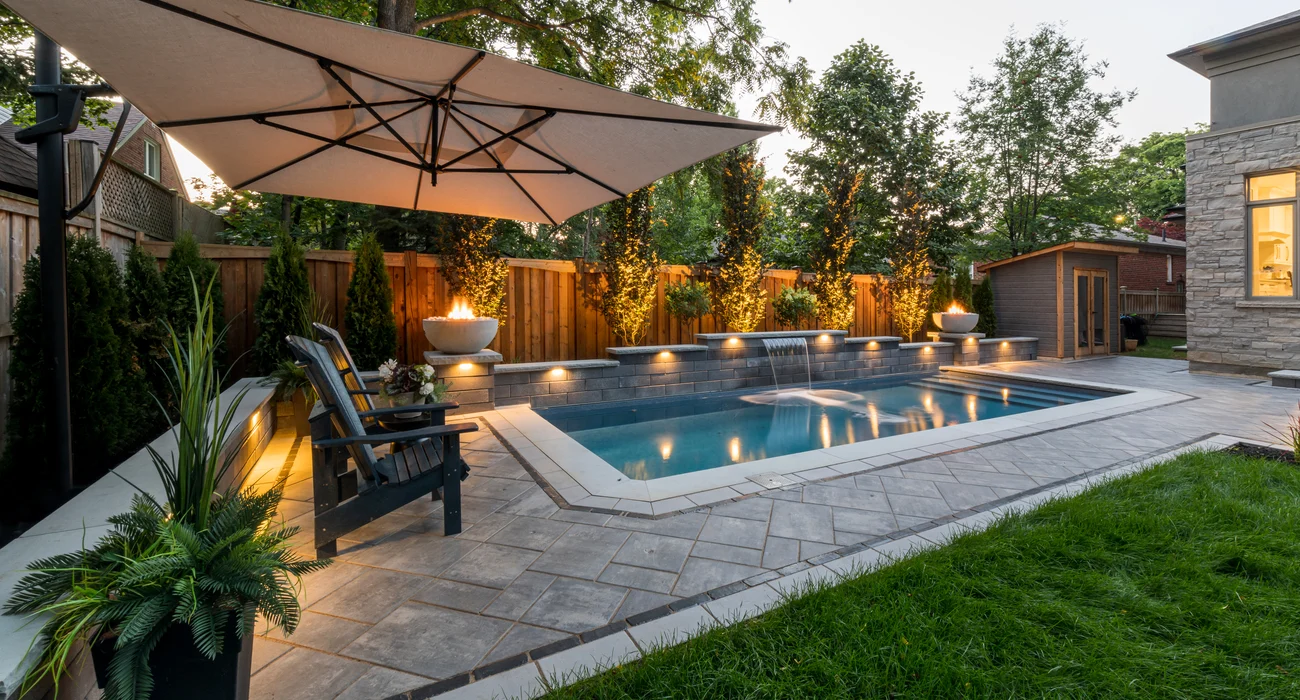 Backyard paver patio with swimming pool and coping. Integrated lighting with fire features