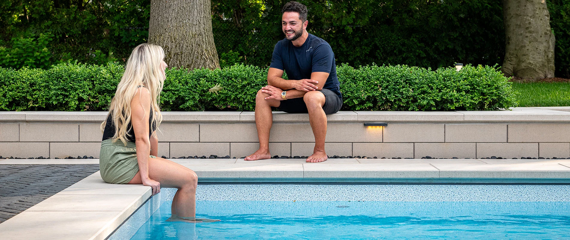 Couple sitting by pool with coping and garden wall