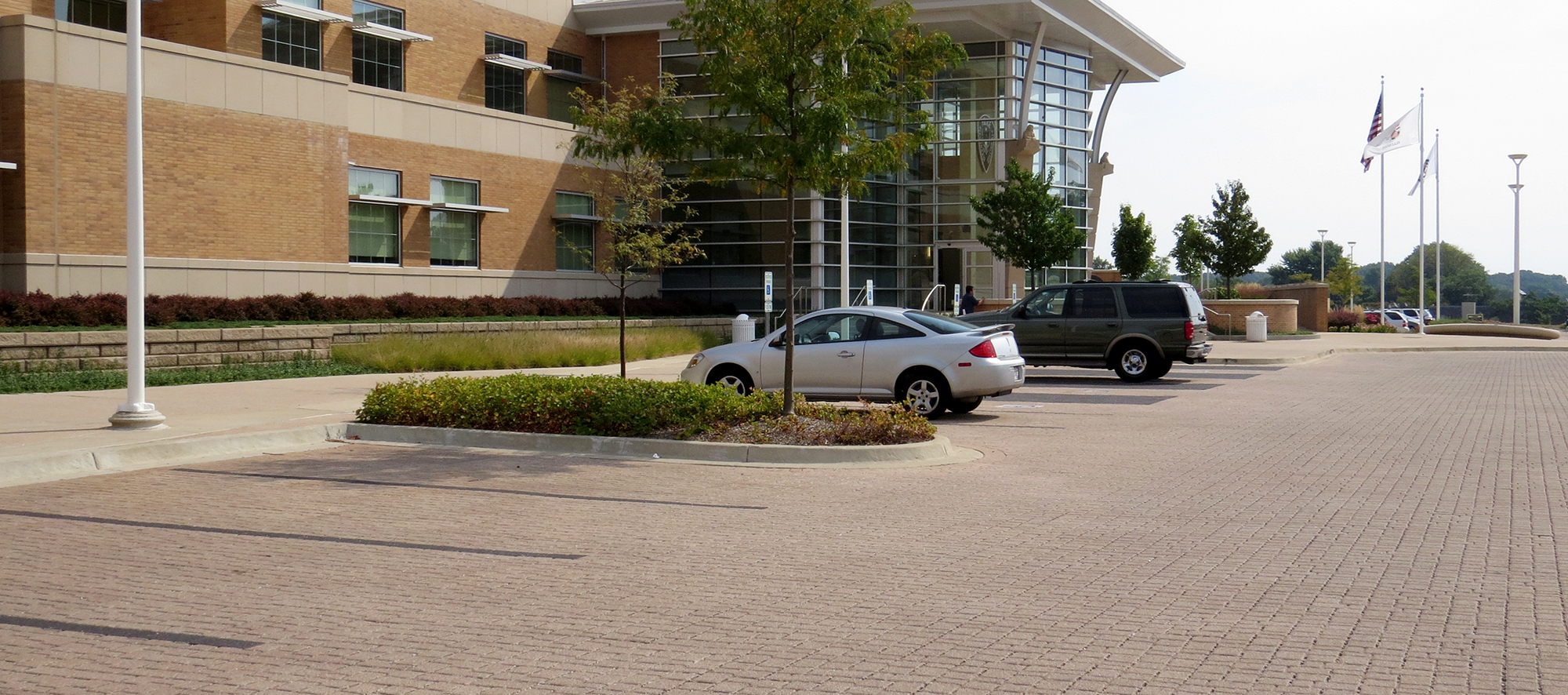 Vehicles in front of a brick and glass building are parked on Eco-Optiloc permeable pavers with dark gray marking the parking spots.