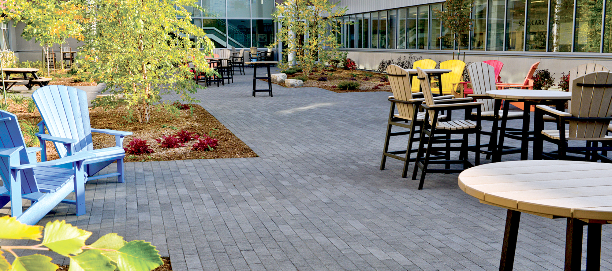 Black Il Campo pavers and modest garden beds help visually elevate surrounding colorful Adirondack chairs and beige tables.