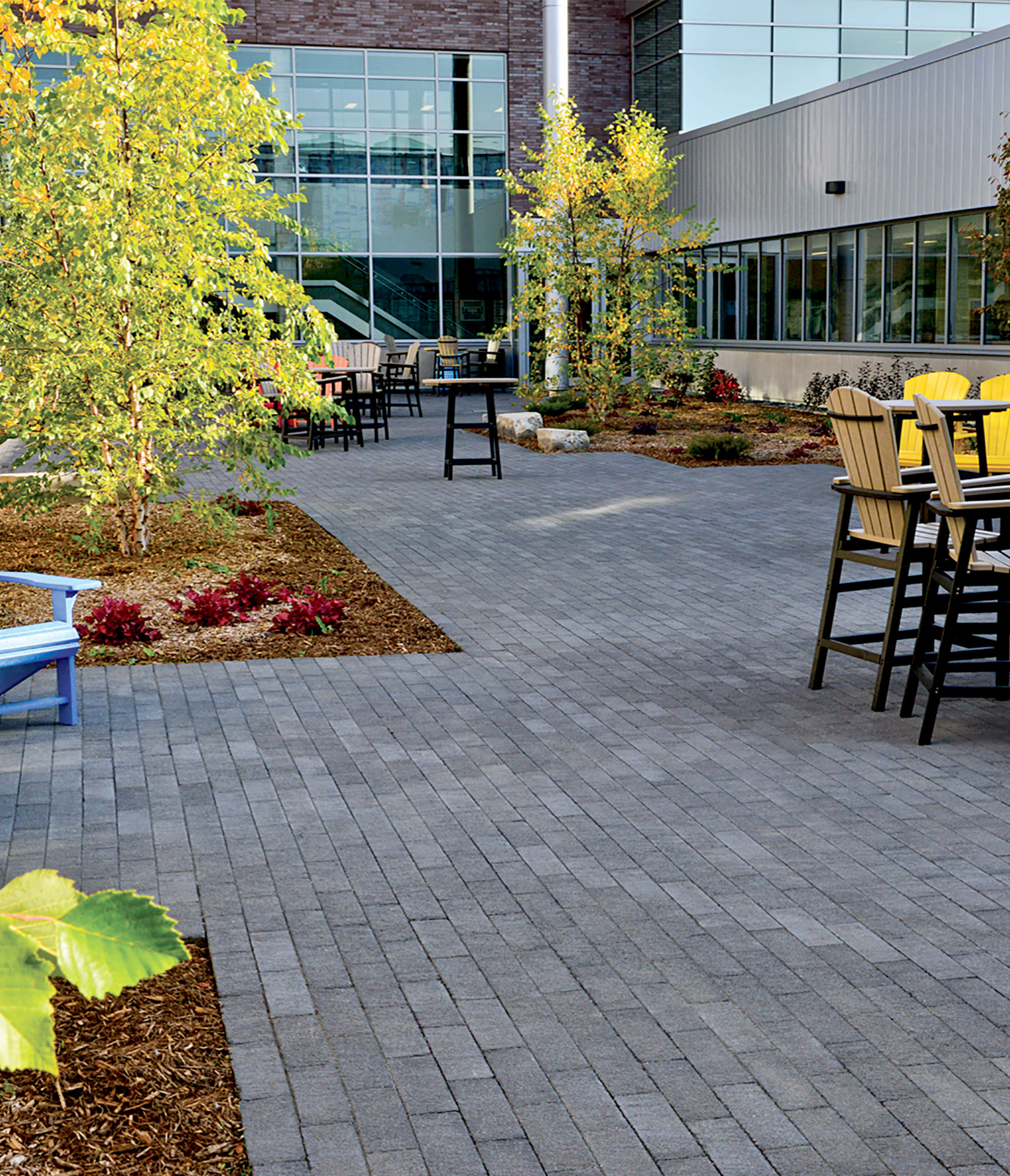 Black Il Campo pavers and modest garden beds help visually elevate surrounding colorful Adirondack chairs and beige tables.