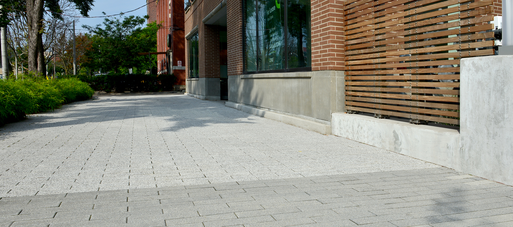 Unilock Promenade Plank pavers in a speckled Umbriano finish sidewalk beside the red brick façade of 400 Wellington condominiums in Toronto.