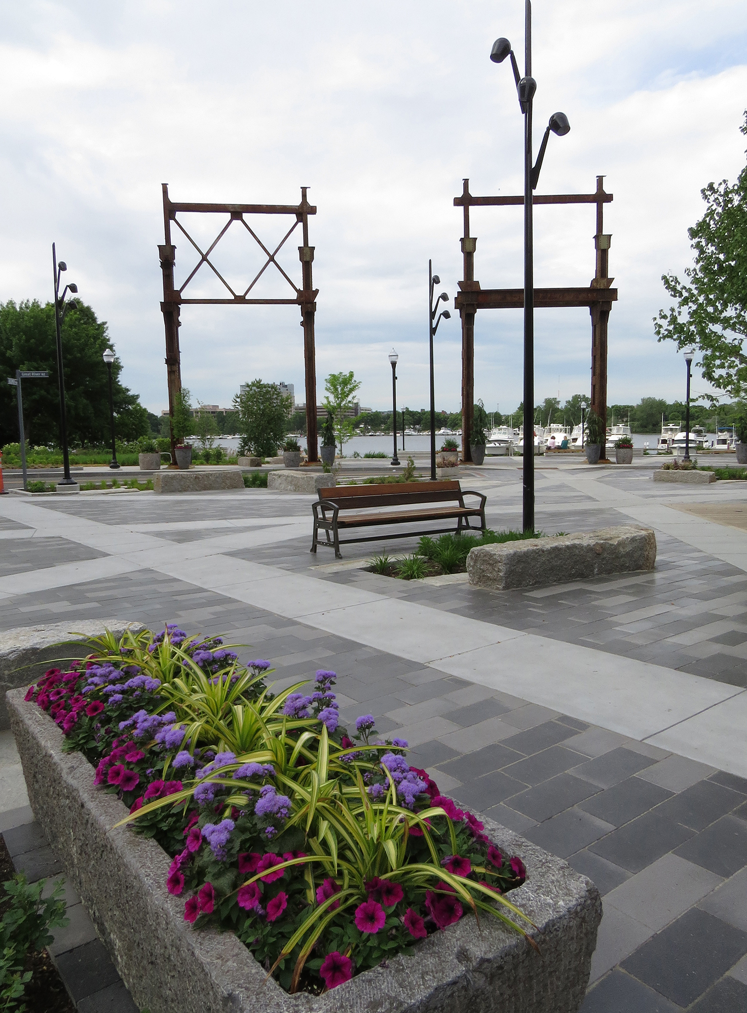 A raised garden with flowers is at the forefront of a waterfront park with unique paving patterns in Senzo pavers and poured concrete.