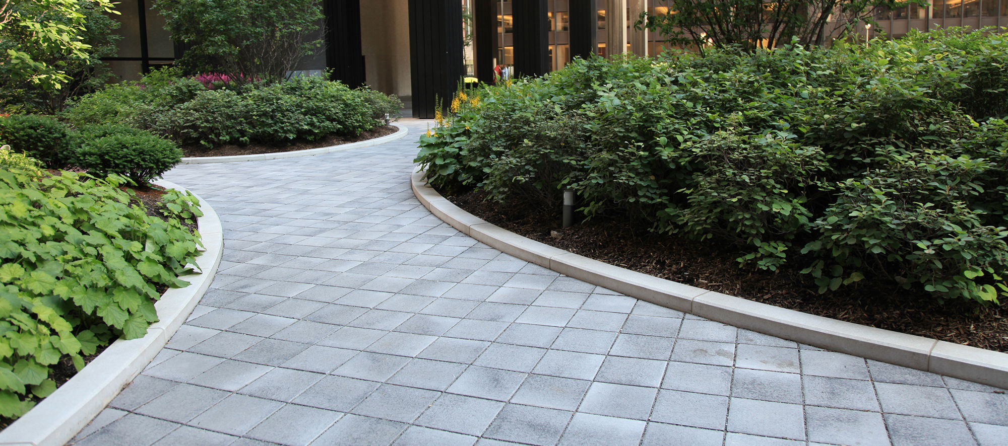 Unilock Umbriano pavers in a custom grey create a curvy walkway and pedestrian area with green space around it, on a condominium roof deck.
