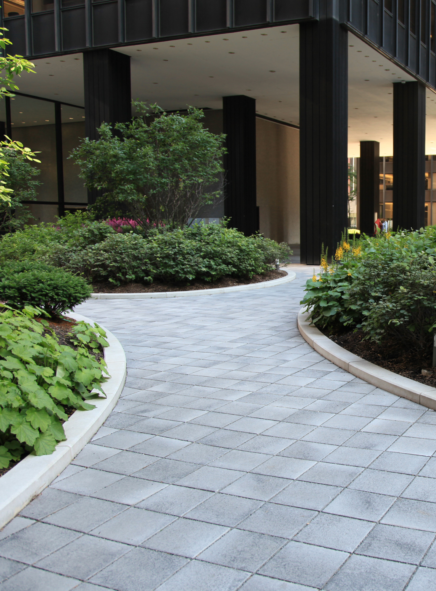 The entrance to a condominium roof deck features Unilock Umbriano pavers in a Custom Grey creating a curvy walkway surrounded by gardens.