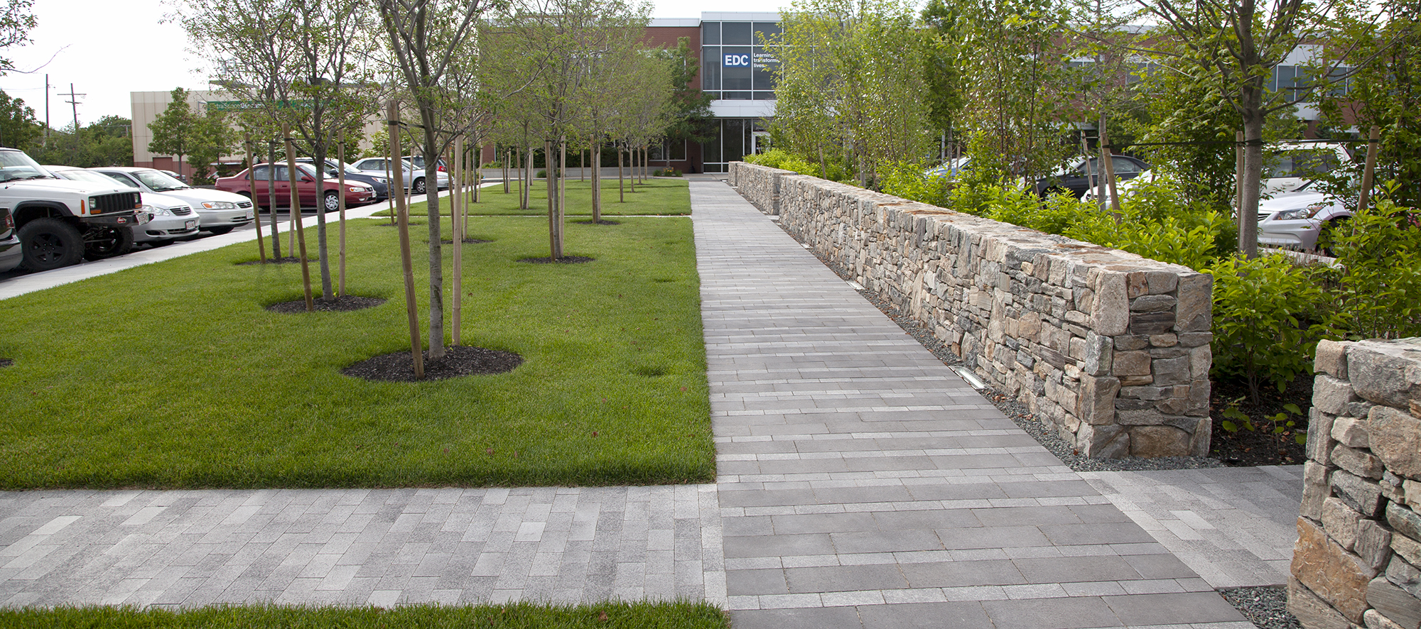 Umbriano pavers alternate between white and grey running parallel with a retaining wall, with more pavers leading to the parking lot.