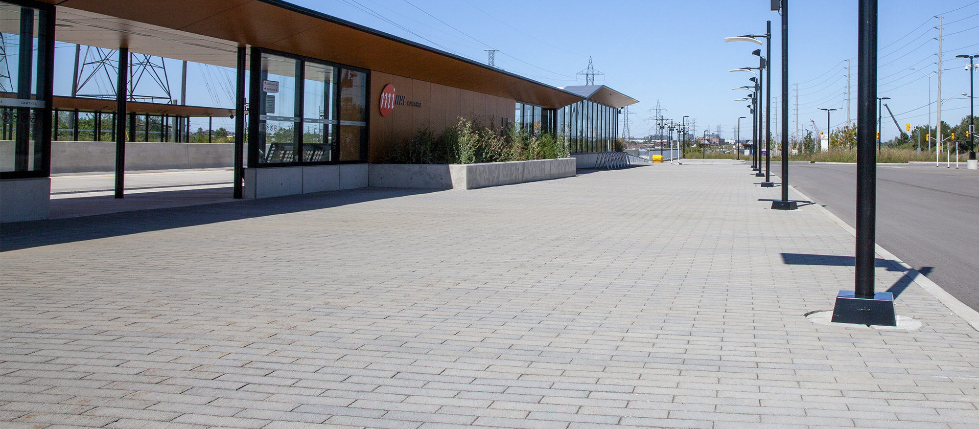 A row of streetlights cast long shadows over a bed of grey Il Campo pavers outside the station's sleek entrance.