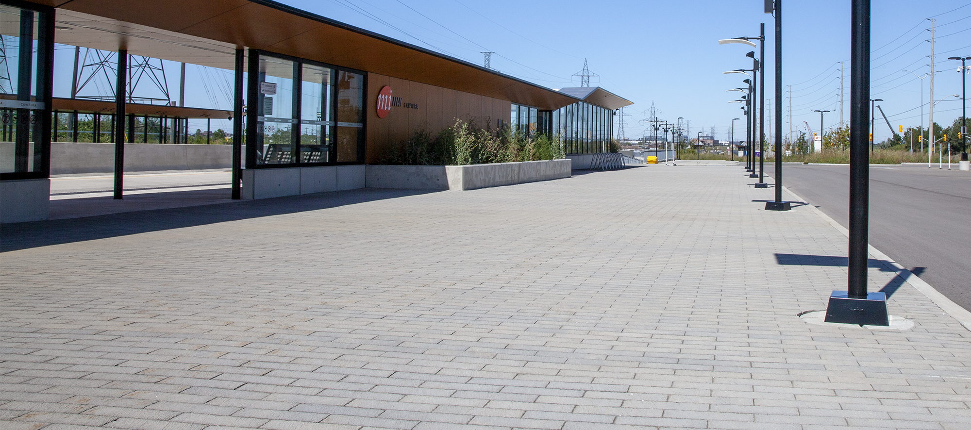 A row of streetlights cast long shadows over a bed of grey Il Campo pavers outside the station's sleek entrance.