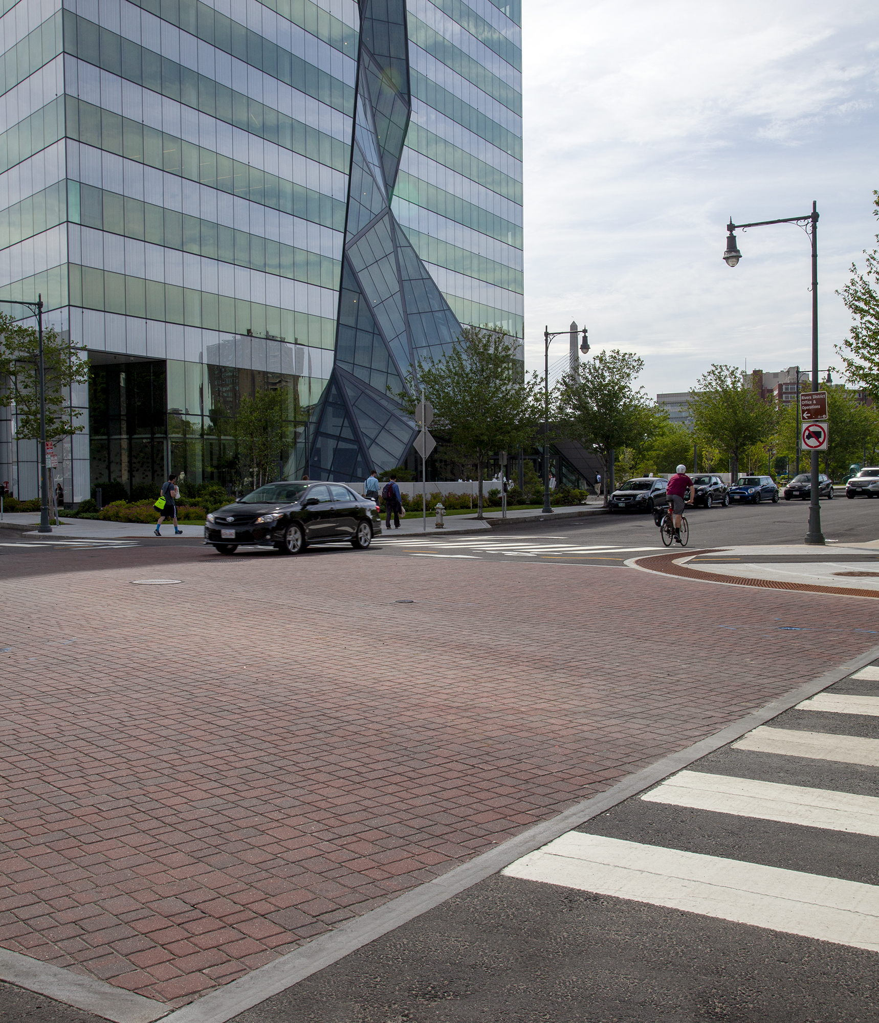 A vehicle, cyclist and pedestrian cross through the intersection, passing over a square paver bed of red Optiloc pavers.