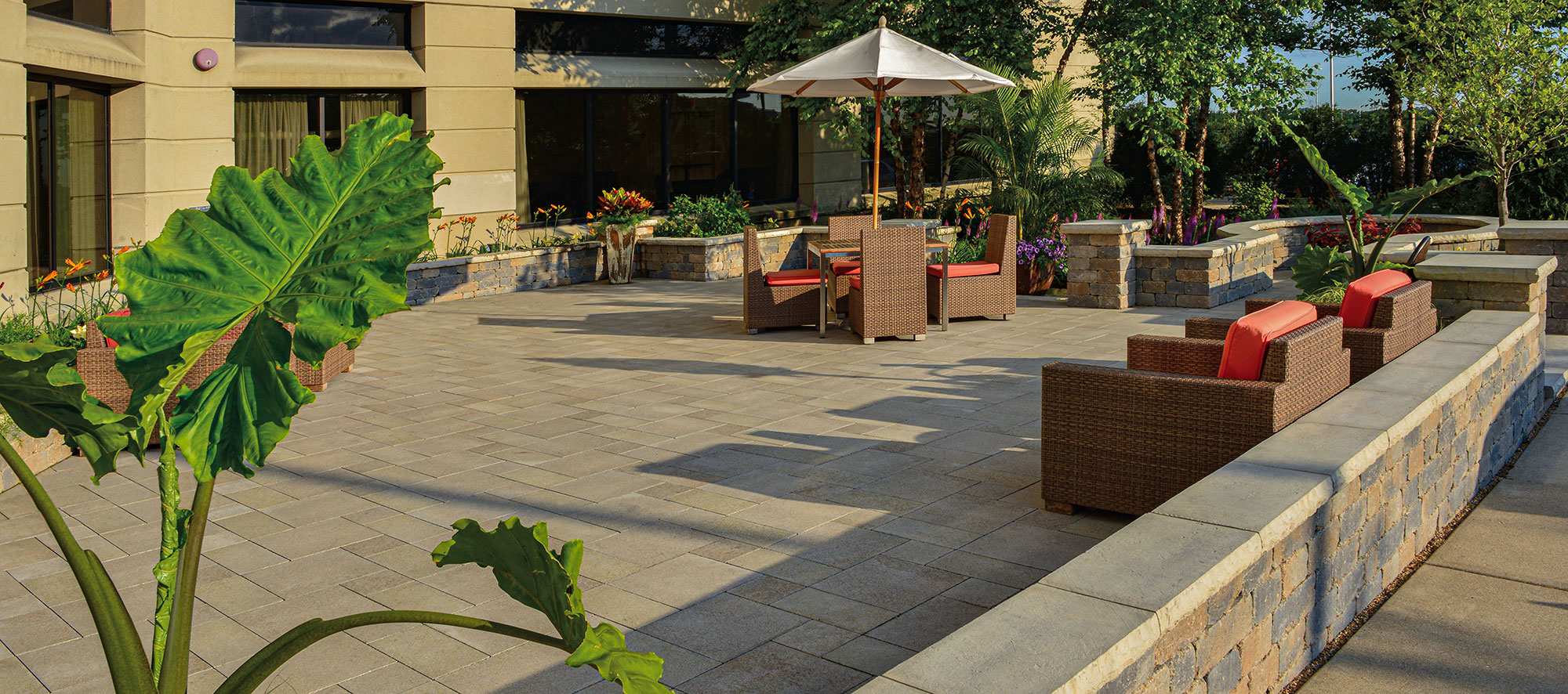 The warm, beige tones of Umbriano make up the main paver floor, with a small retaining wall and patio furniture strewn throughout the space.