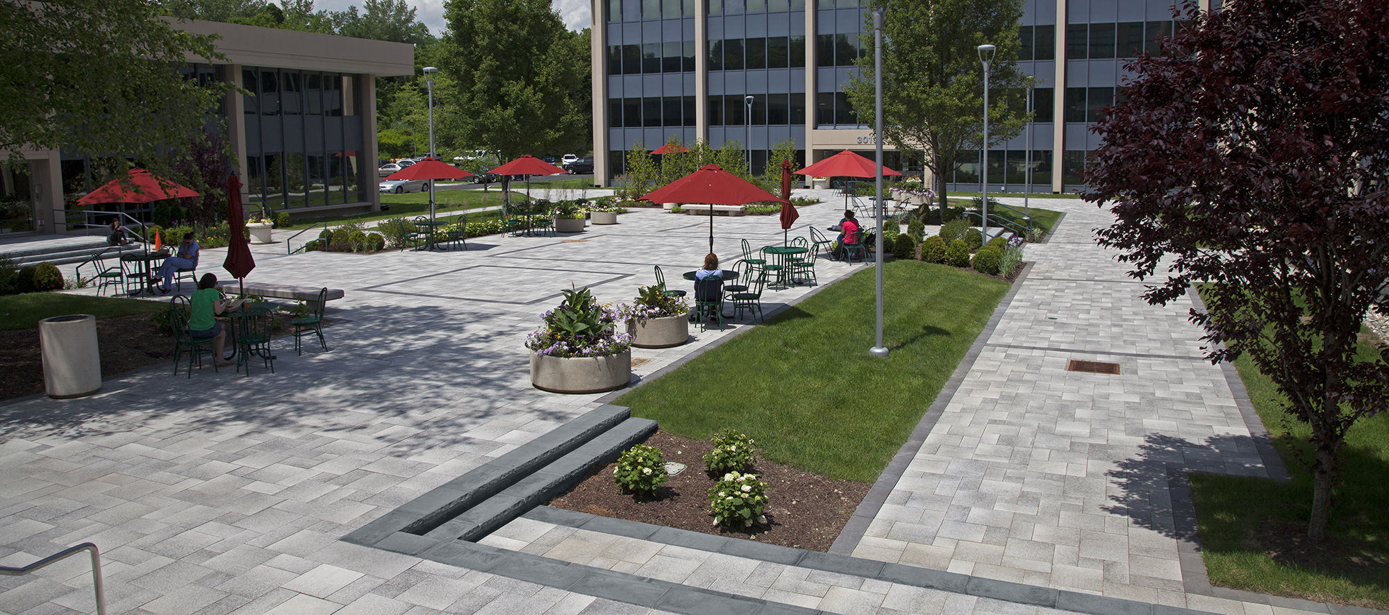 Umbriano pavers visually enhance colorful elements around the plaza, including garden beds, planters, tables, chairs, and umbrellas.