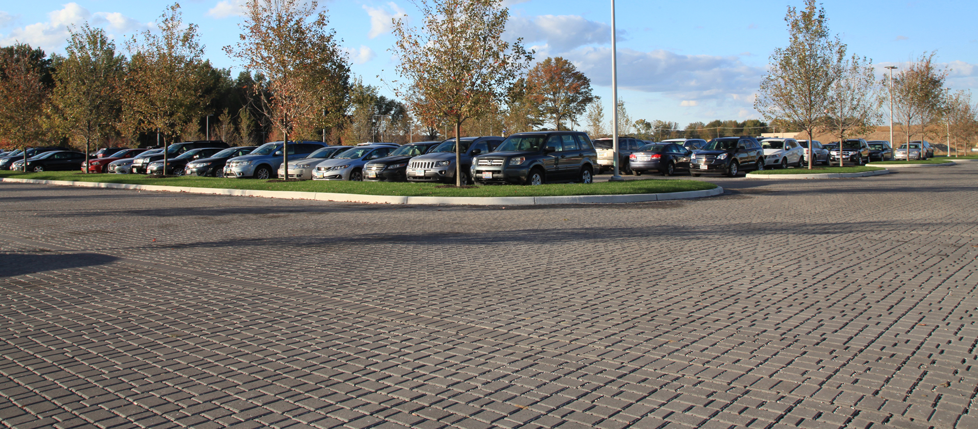 Motor vehicles occupy a busy parking lot at the Cleveland Clinic, featuring a warm dark grey hue of Eco-Optiloc pavers throughout the space.
