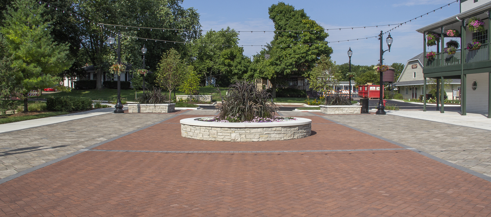 Surrounded by trees and grass, Unilock pavers in contrasting colors create a pedestrian area with a circular walled garden in the middle.