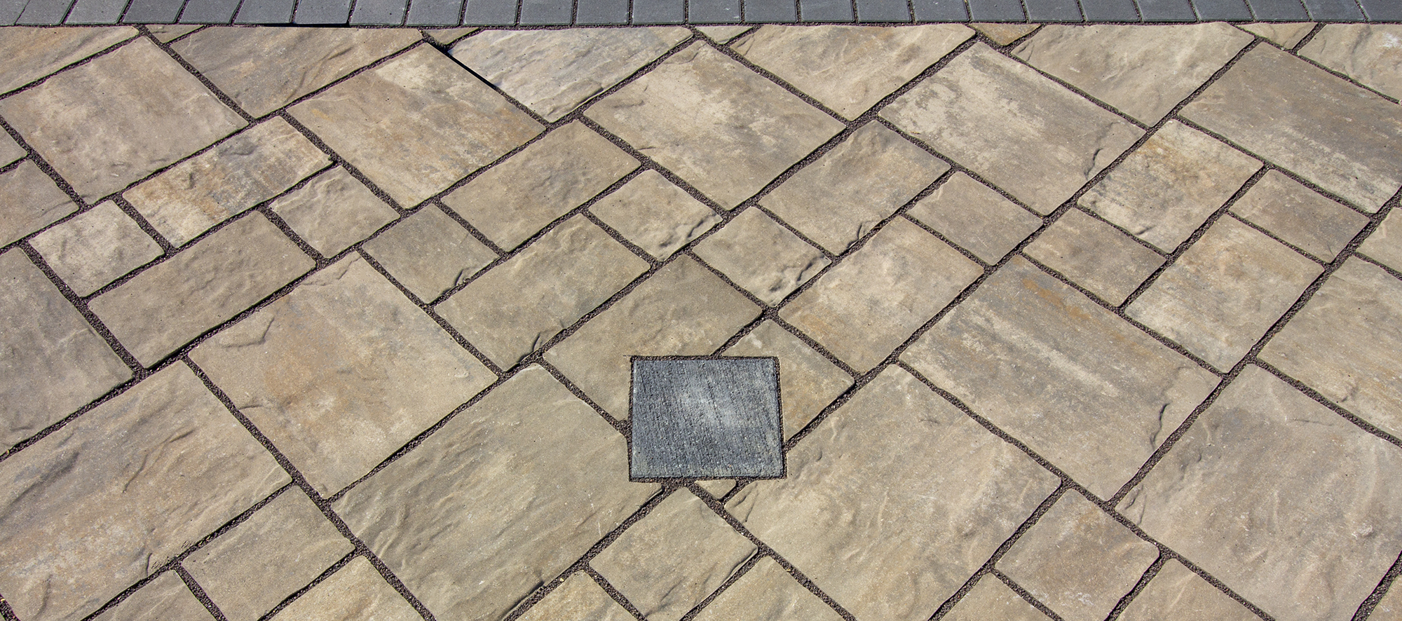 Thornbury pavers with a textured finish in beiges and warm browns with a small dark drey square with a brushed finish.