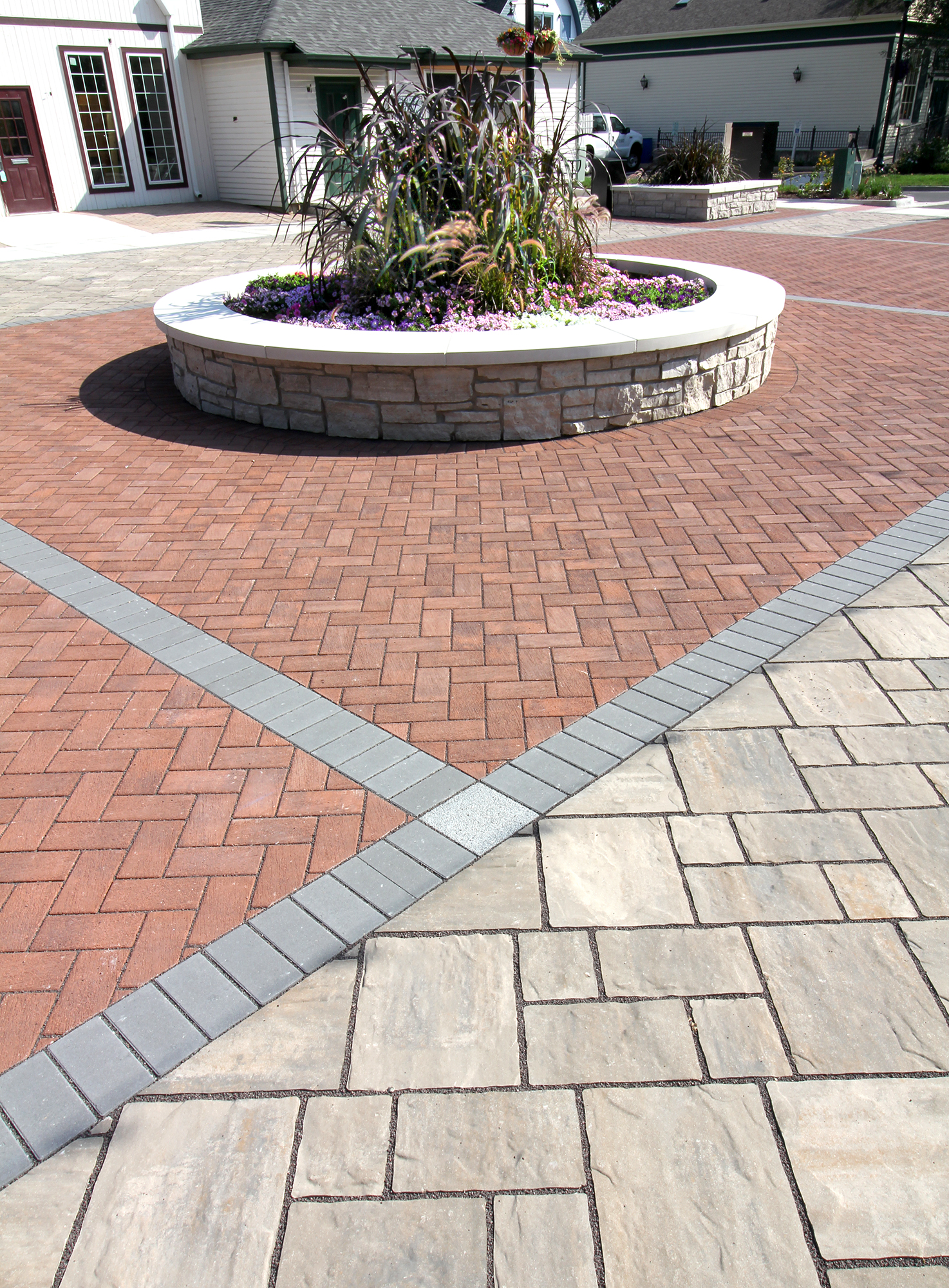 Unilock pavers in geometric shapes and contrasting colors create a pedestrian area with a circular walled garden in the middle.