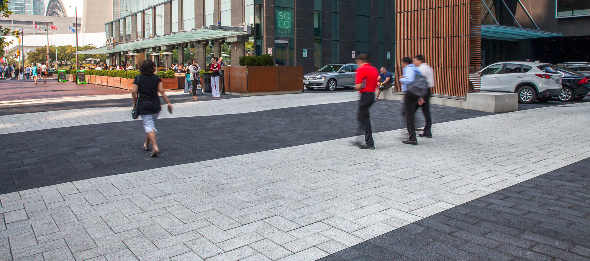 In front of the Delta Hotel Toronto, people walk on bold stripes of Series pavers in contrasting colors, laid in a herringbone pattern.