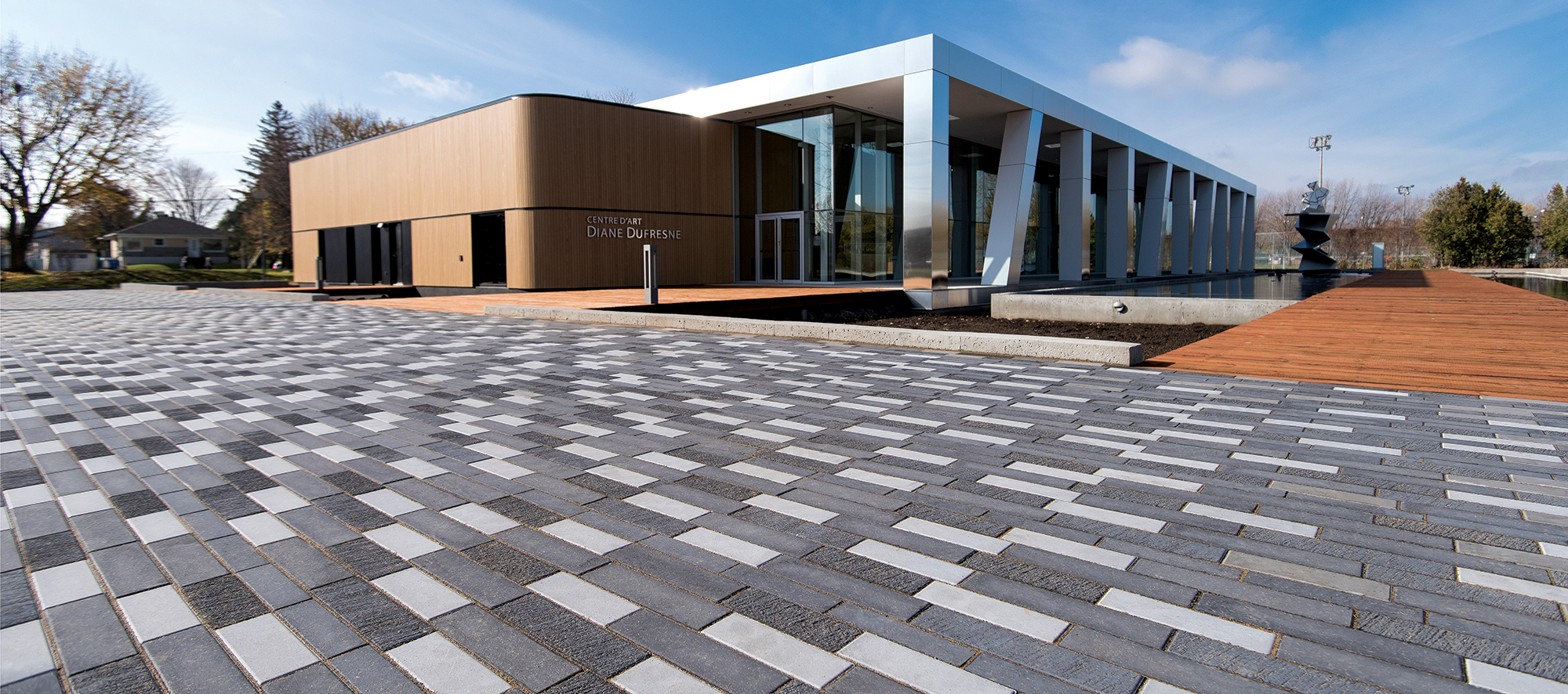 Tri-colored Il Campo pavers cohesively blend with the beige and chrome architecture of the building, bordered by boardwalk style walkways.