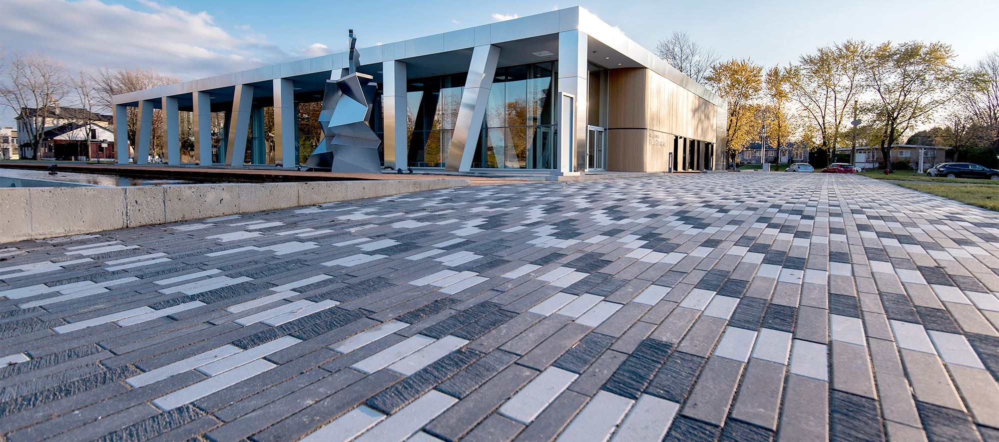 The textures of Il Campo pavers shine under the light of the sun, with a stunning art piece on display outside the building entrance.