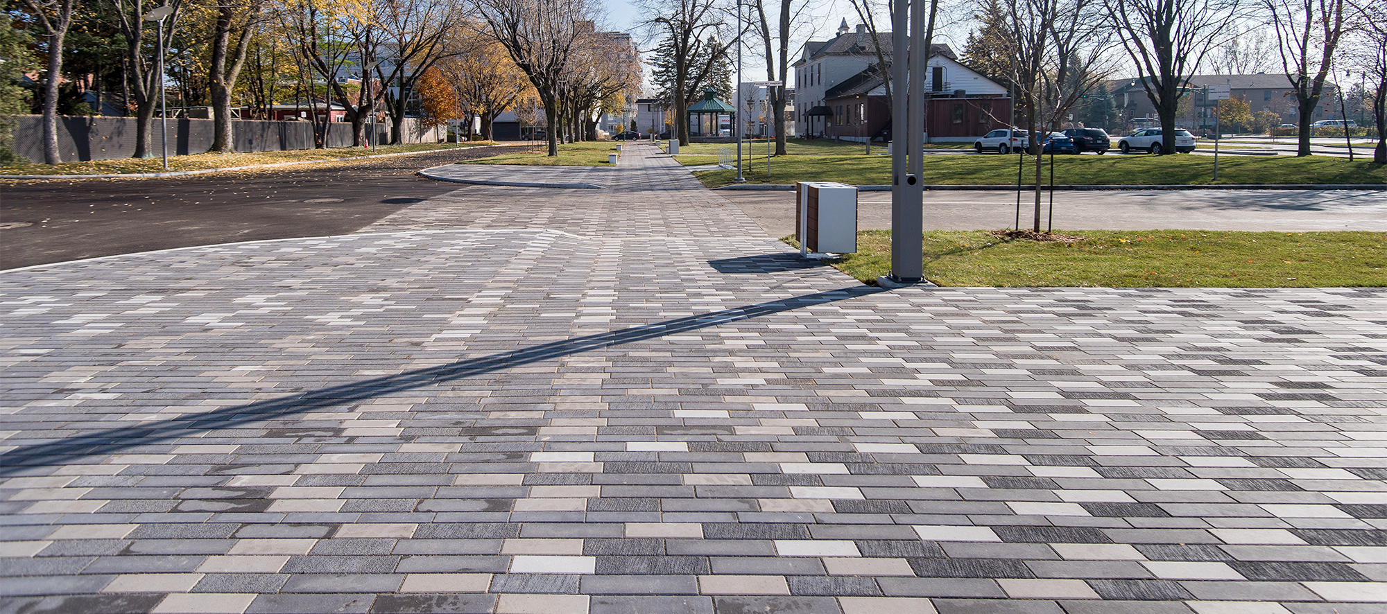 Tri-colored Il Campo pavers stretch the length of the street, bordered by grass and trees, and the road.