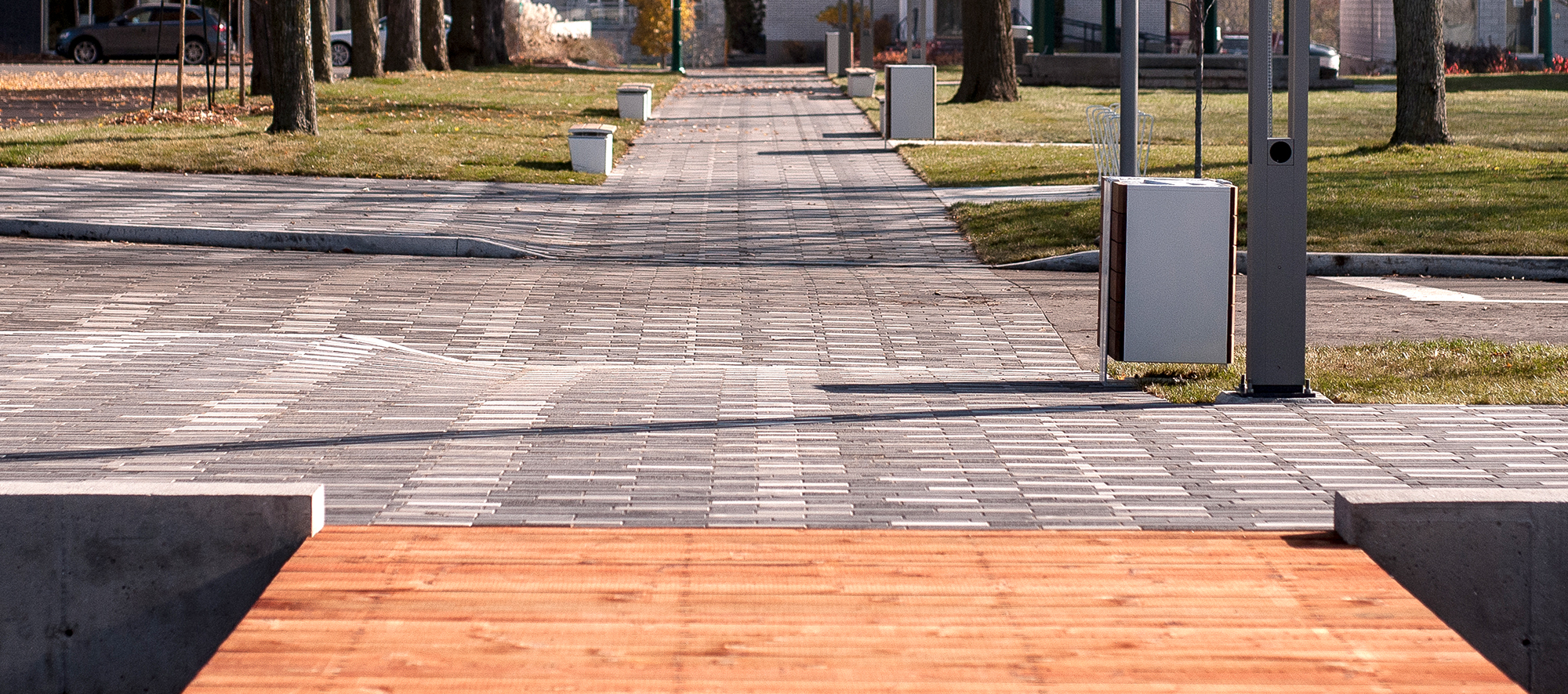 A boardwalk-style walkway transitions to tri-colored Il Campo laid horizontally moving left and right toward the road.