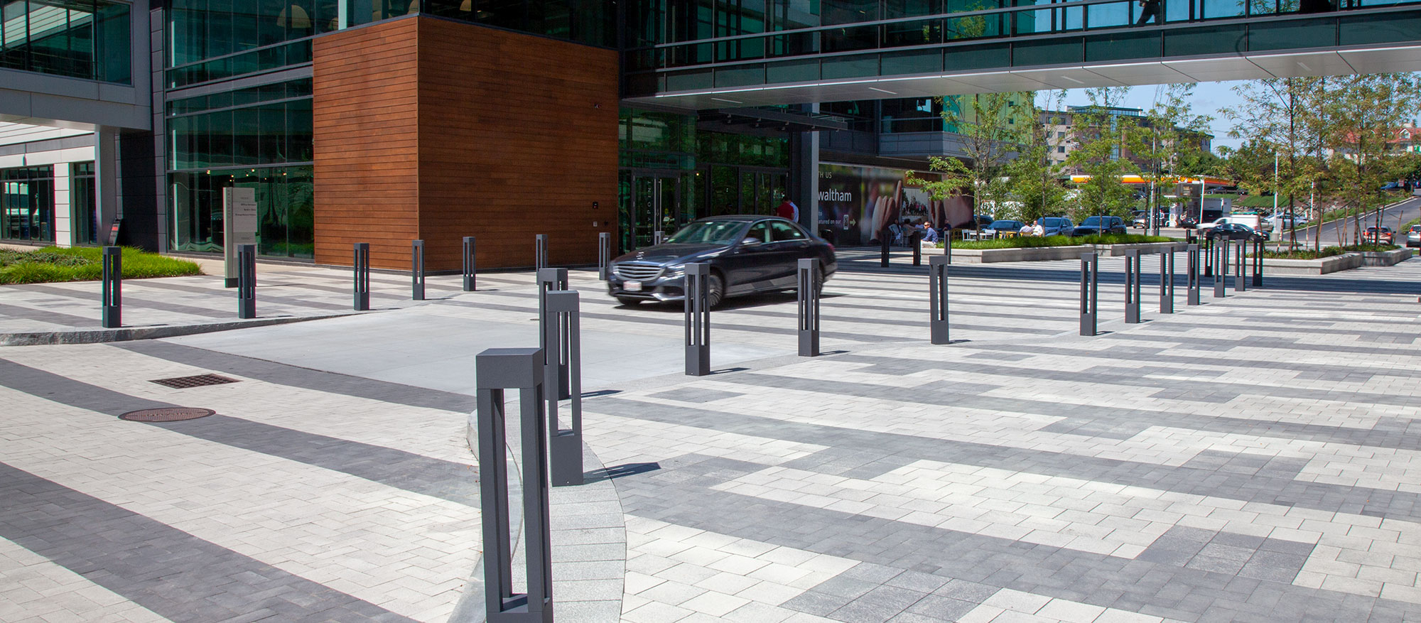 Unilock Umbriano pavers in contrasting colors and patterns delineate areas for pedestrians and cars between buildings connected by a bridge.