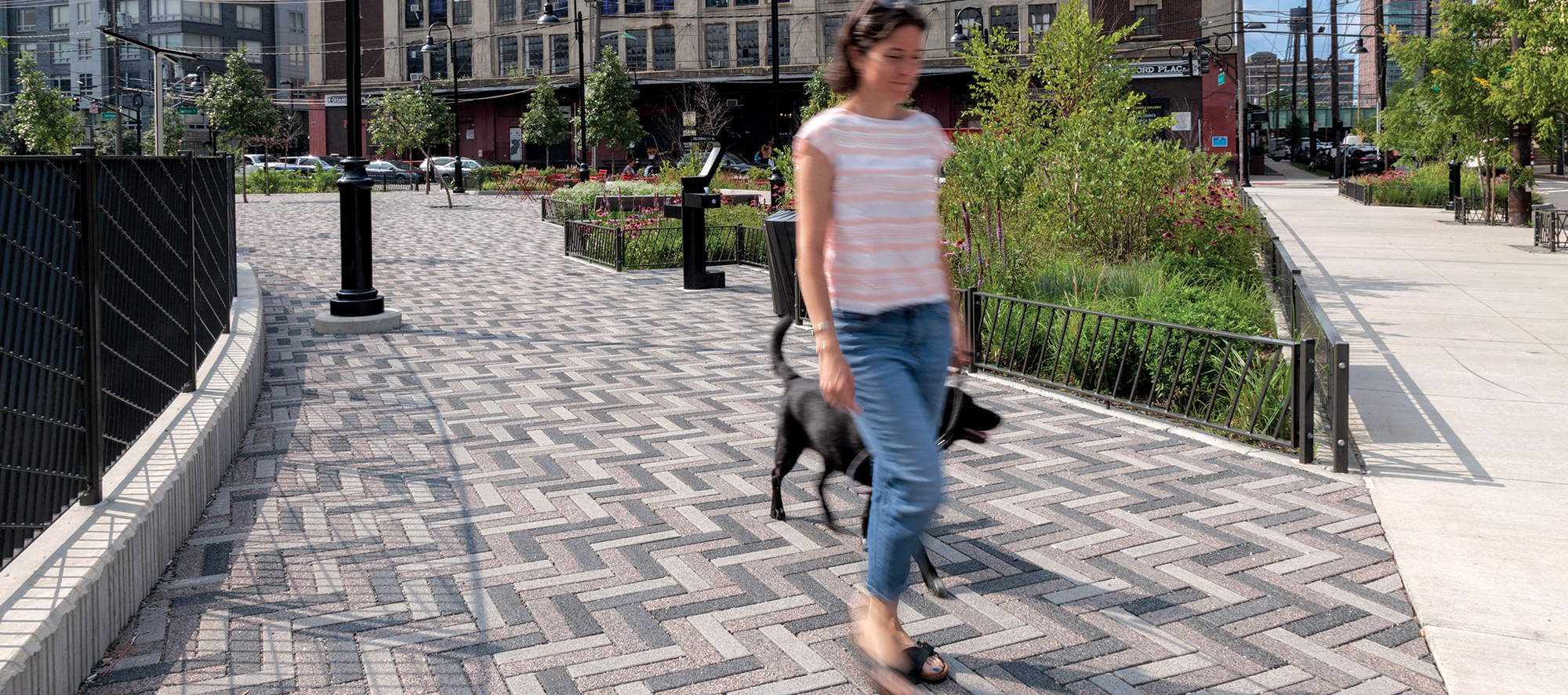 A person walks a dog along a route with Eco-Promenade pavers in three distinct hues arranged in a zigzag pattern to add visual interest.