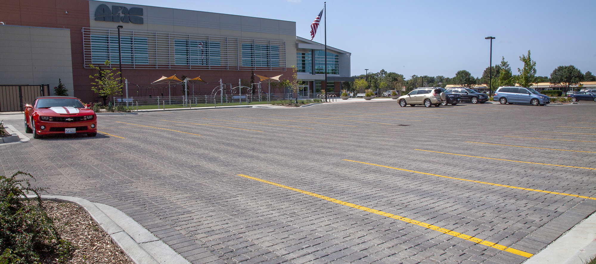 The parking lot of an Athletic and Recreation Center with Eco-Optiloc permeable pavers in Natural with yellow lines marking where to park.