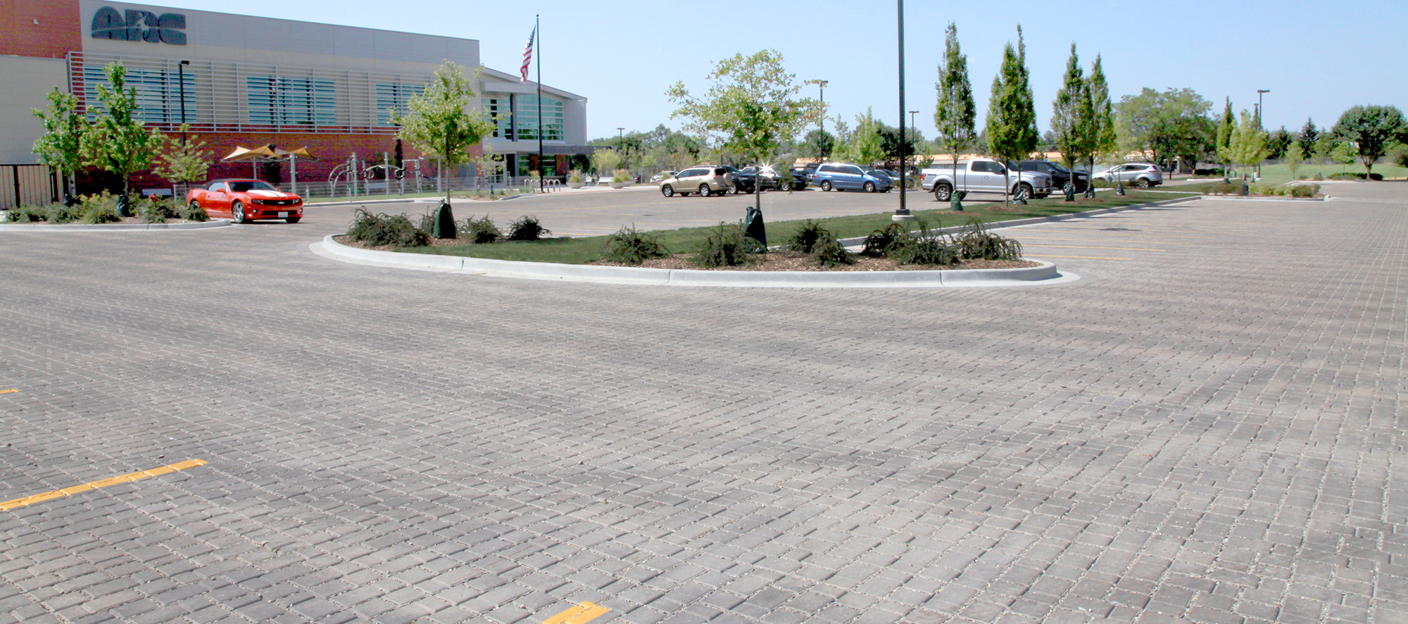 Cars park in the parking lot of an Athletic and Recreation Center, paved with Eco-Optiloc permeable pavers around shaped raised garden beds.