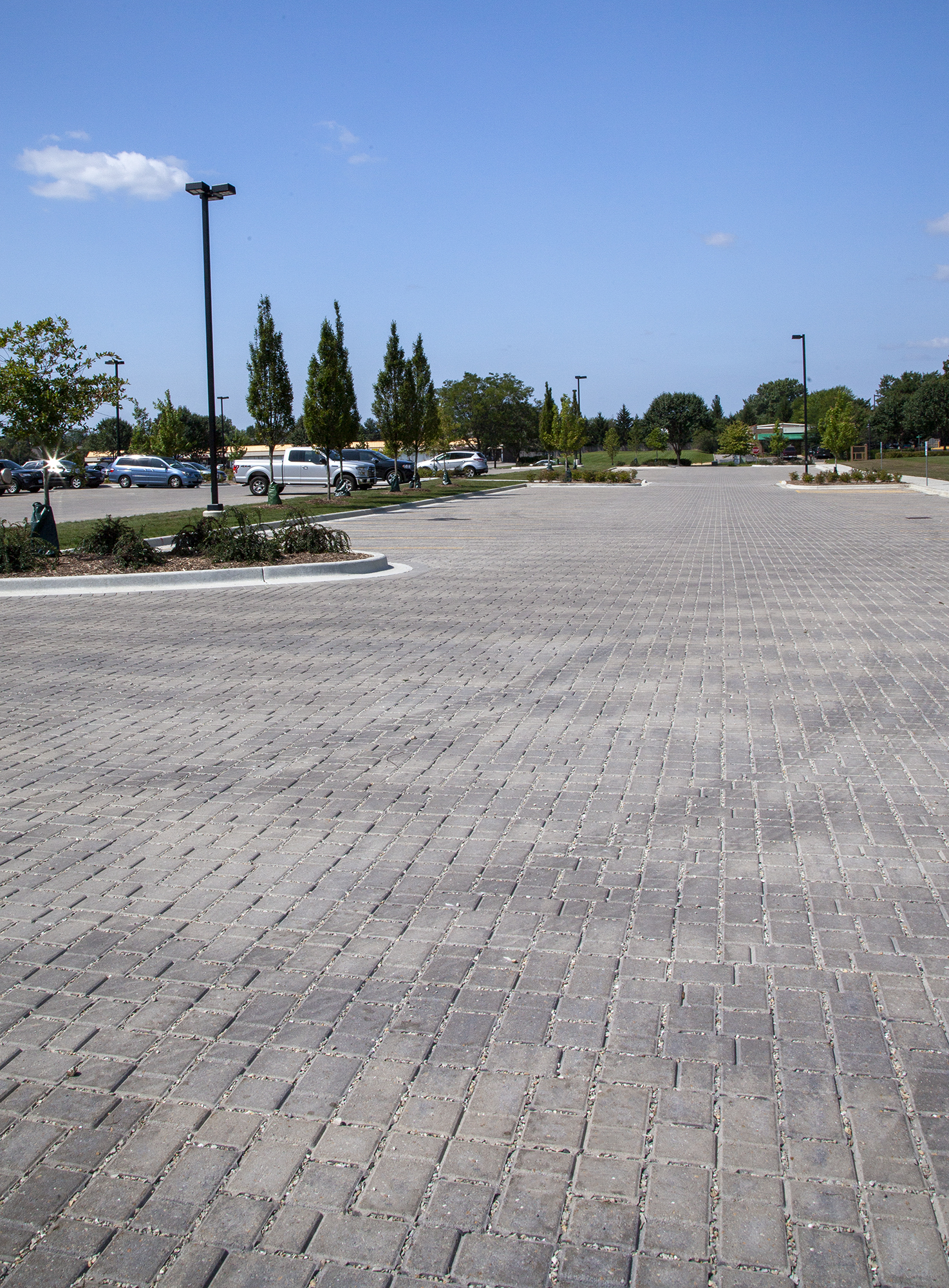 Cars in the parking lot of an Athletic and Recreation Center paved with Eco-Optiloc park around shaped raised garden beds.