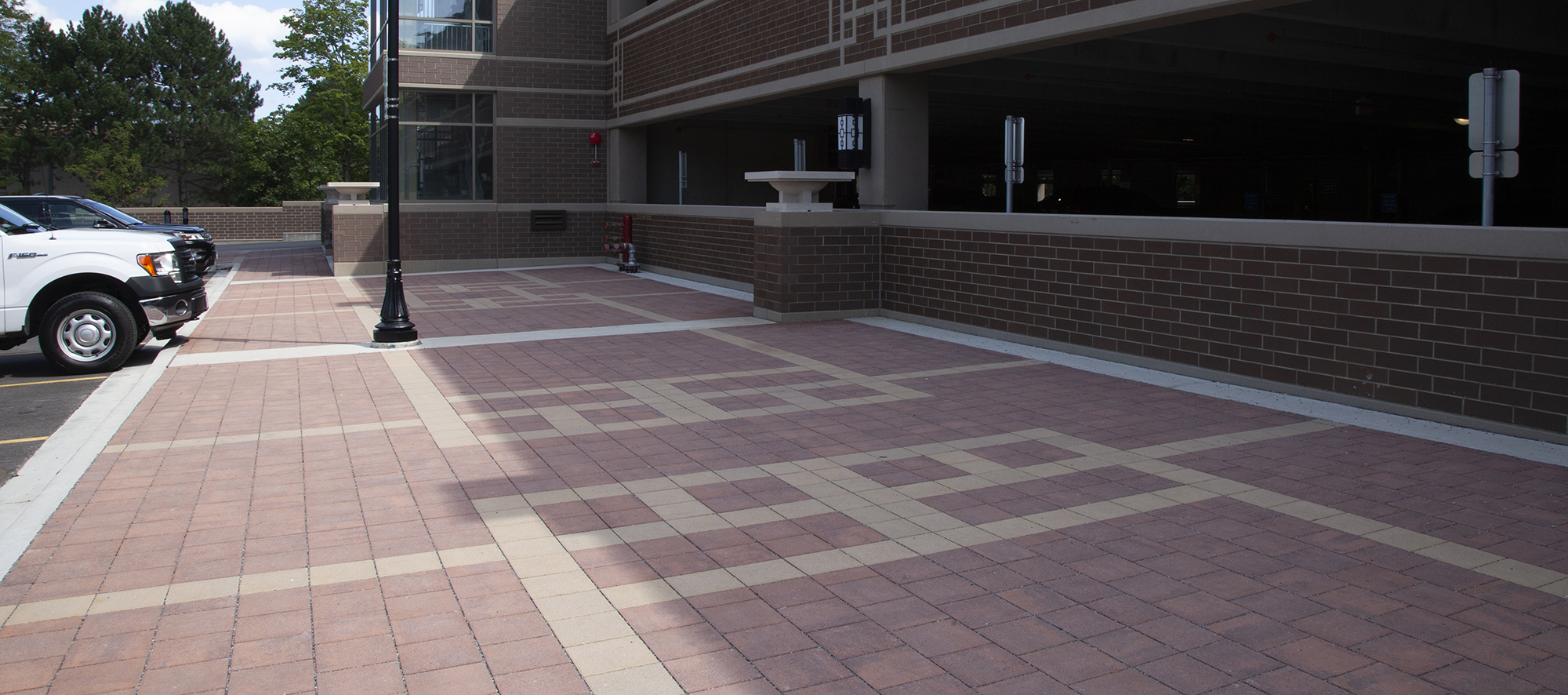 Red and beige Eco-Priora pavers form unique, shapely patterns against the red brick exterior of the enclosed parking lot.