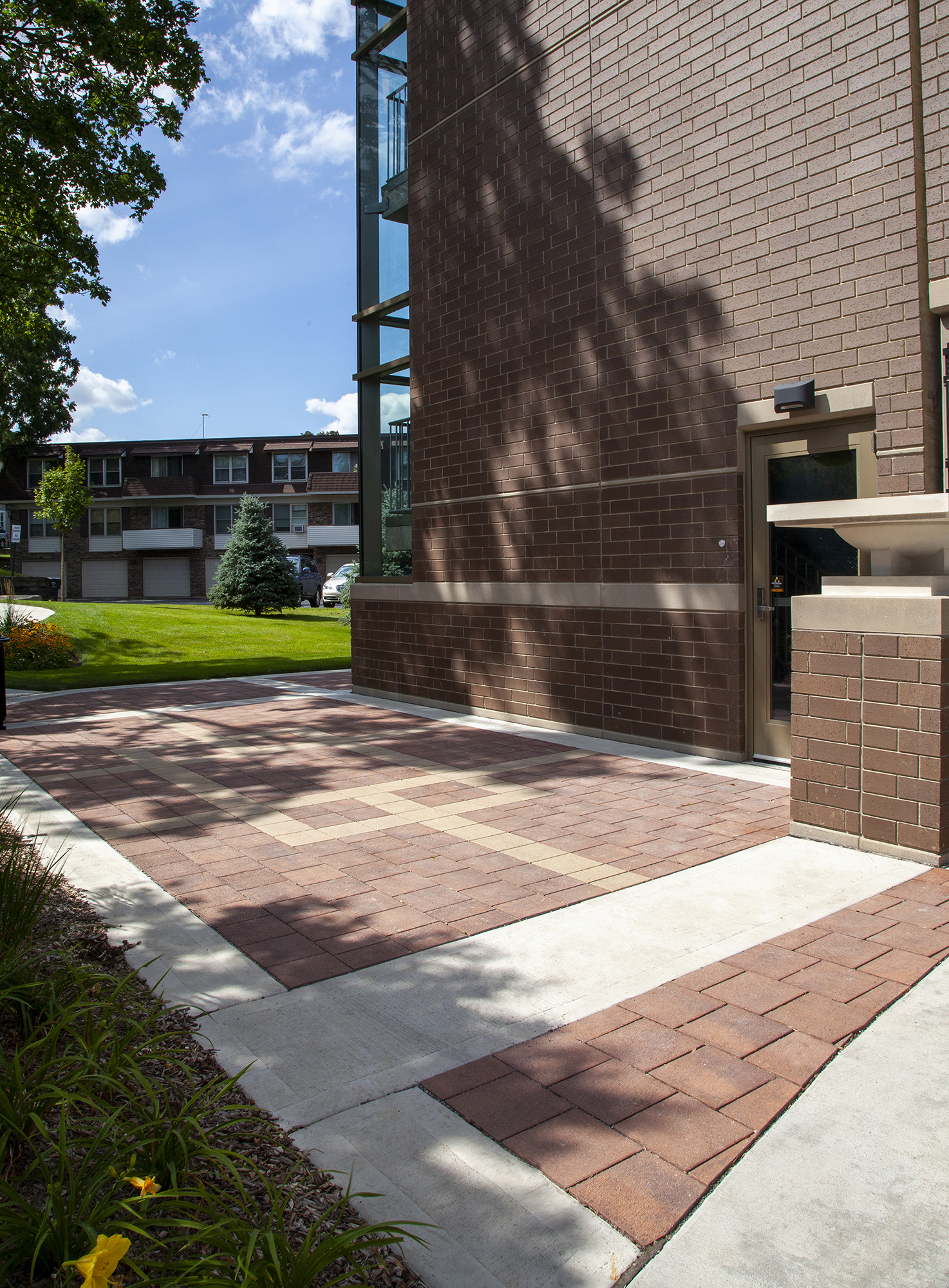Red and beige Eco-Priora pavers continue around the cornerr of a brick building, matching the red brick exterior.