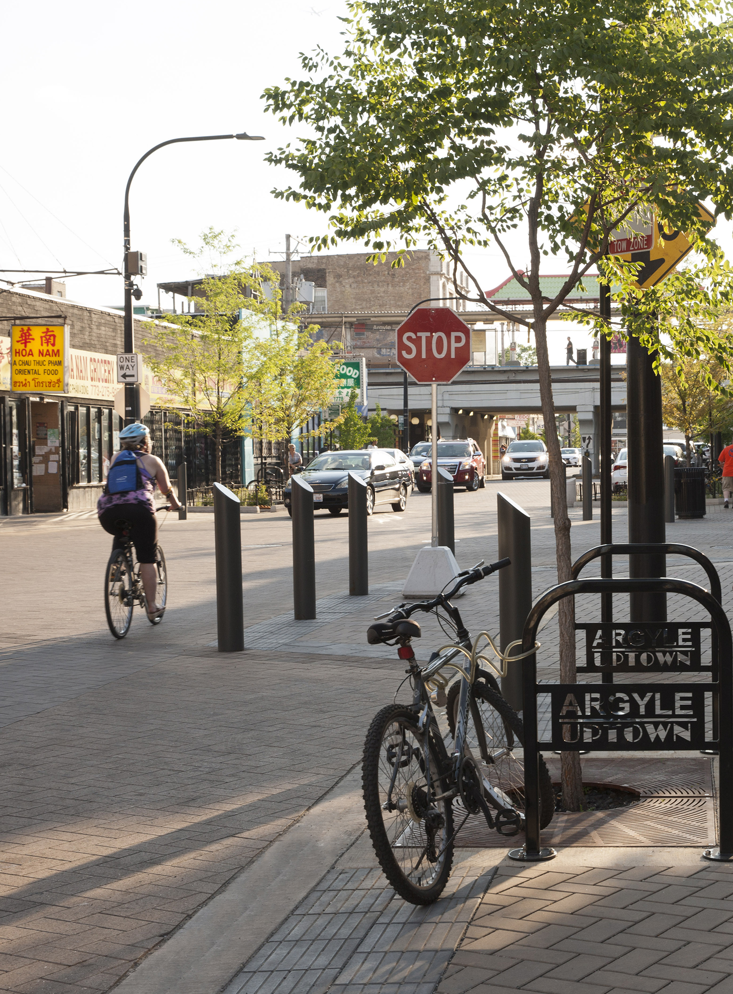 A cyclist bikes past cars on a streetscape paved with Unilock Eco-Priora permeable pavers. A bike rack has the words 