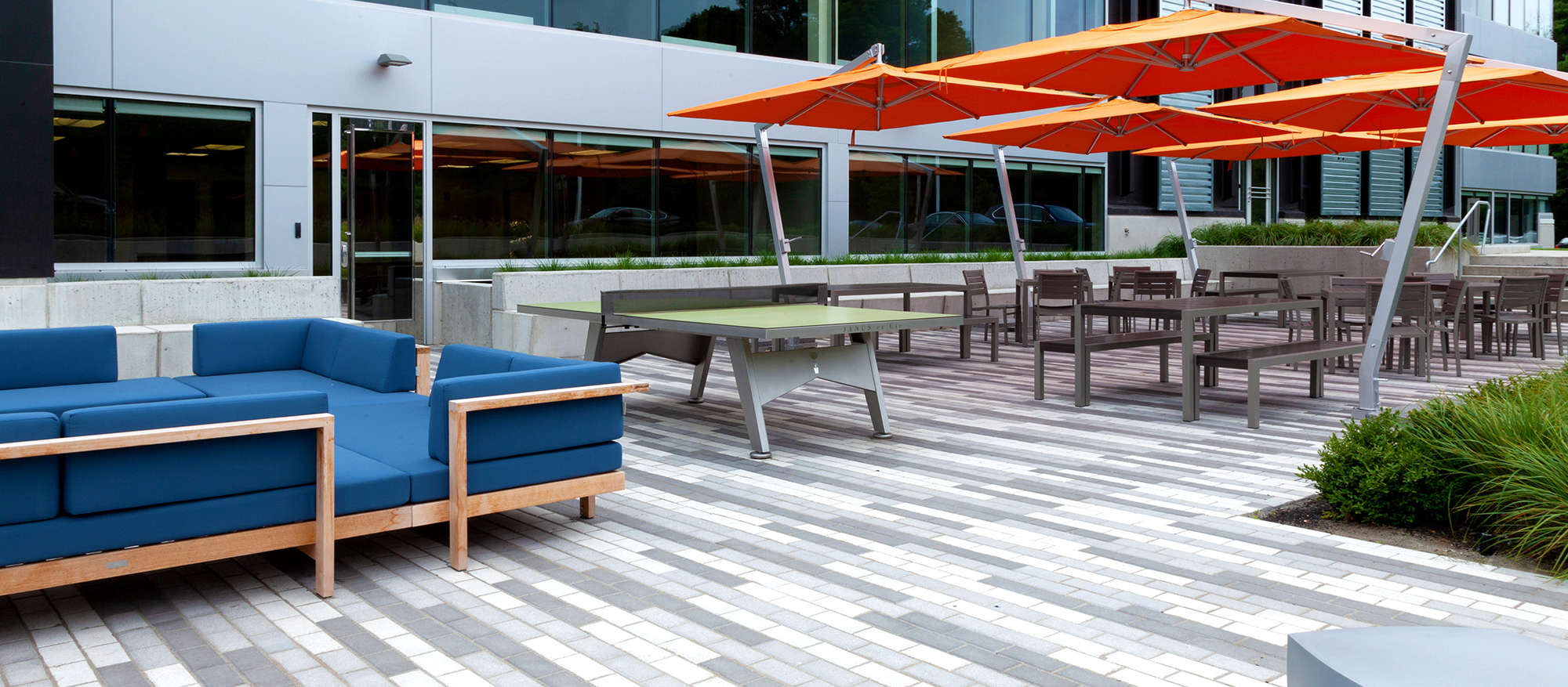 An outdoor amenity area features a 3 color linear pattern made from Unilock pavers, outdoor furniture, and large orange umbrellas.