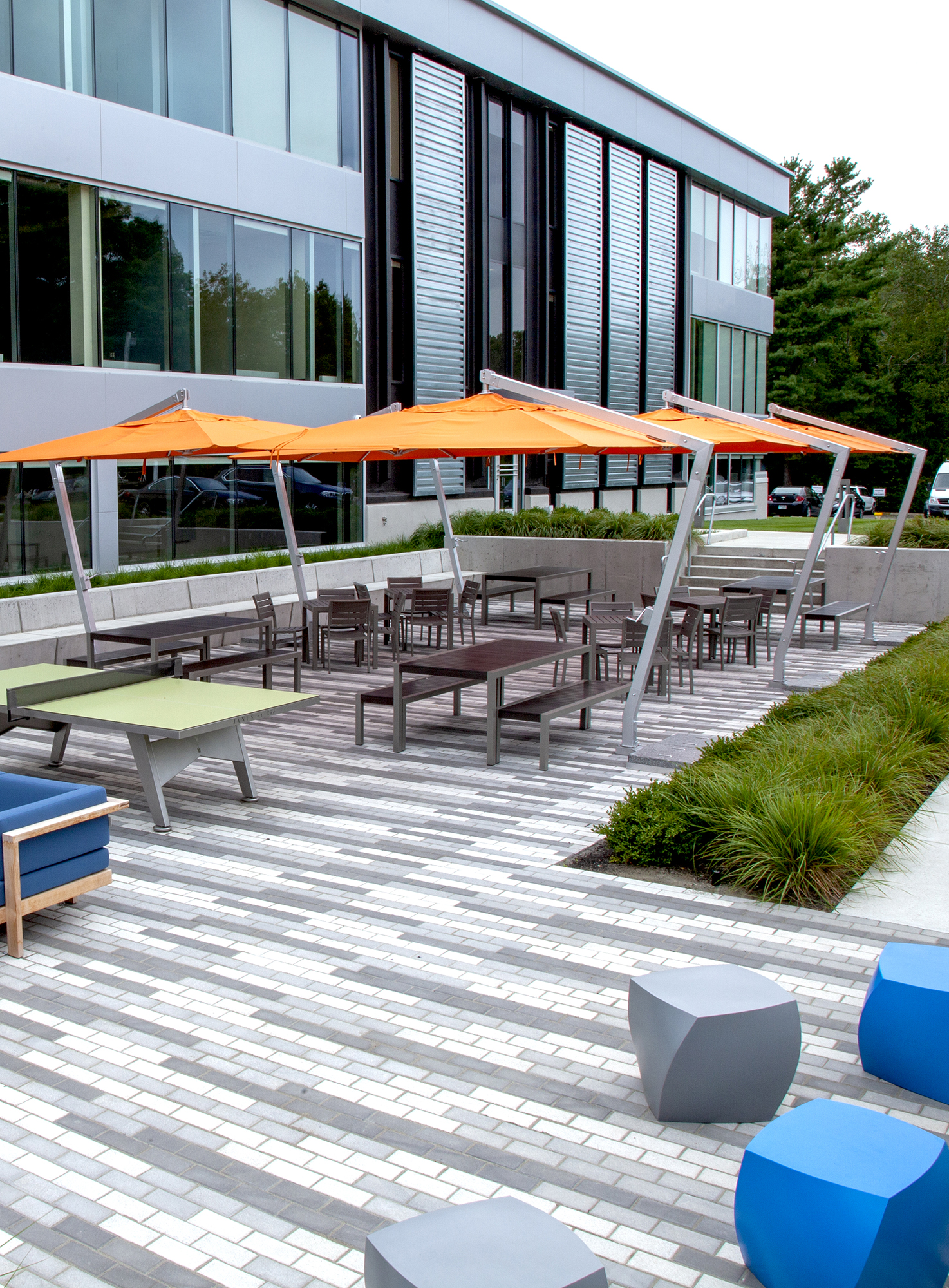 An outdoor amenity area features a 3 color linear pattern made from Unilock pavers, outdoor furniture, and large orange umbrellas.