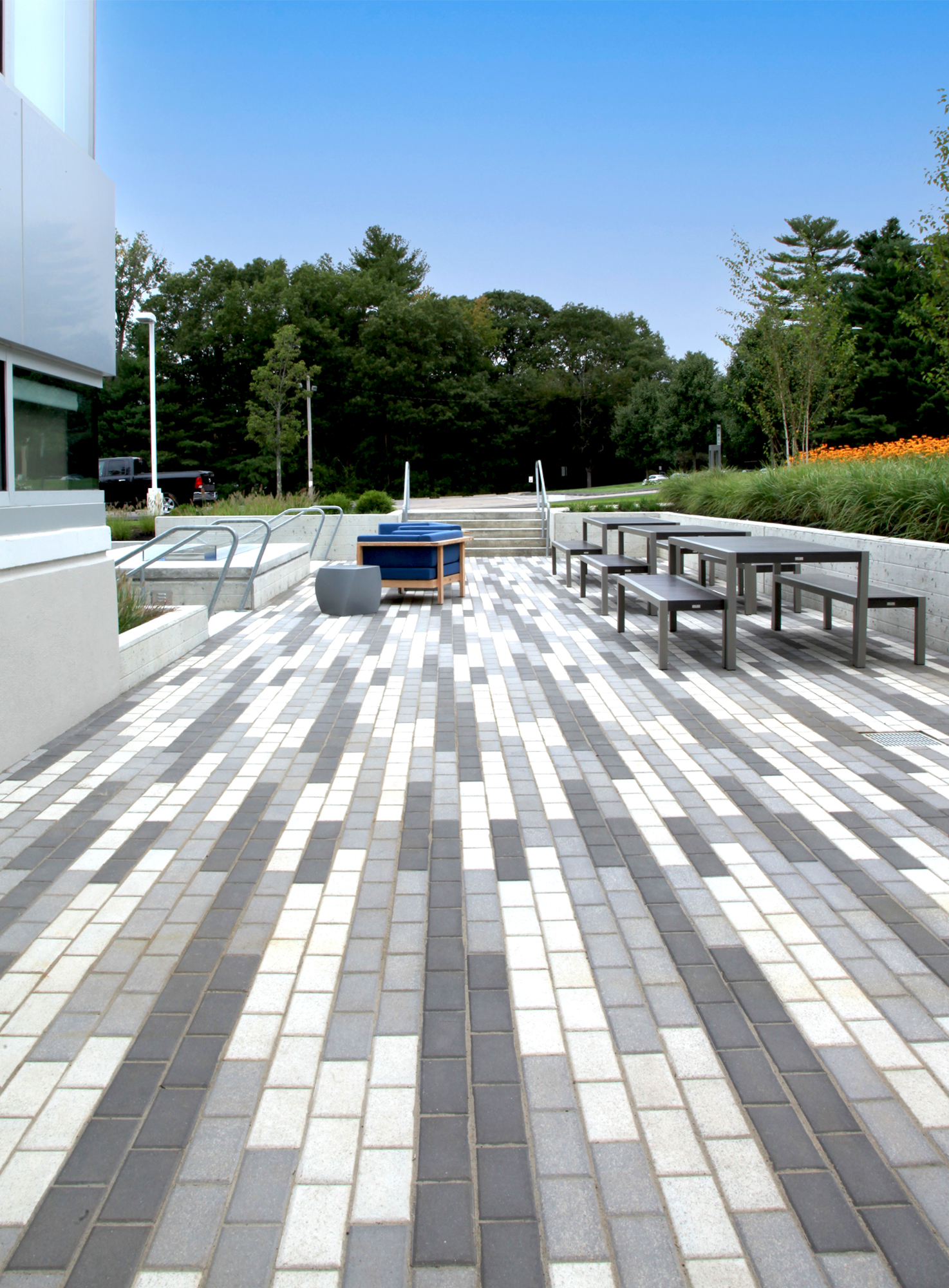 This outdoor amenity area features a 3 color linear pattern made from Unilock Umbriano pavers, modern furniture, and large orange umbrellas.