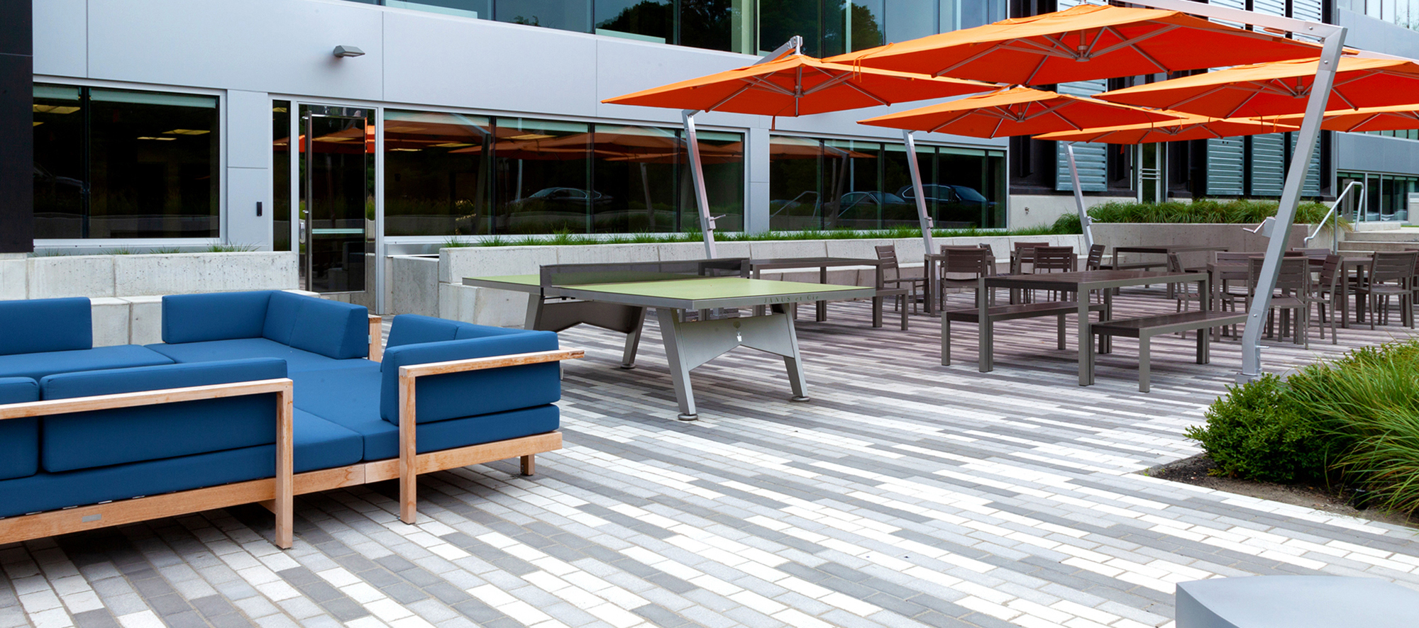 180 Wells Ave. outdoor amenity area features a 3 color linear pattern made from Unilock Umbriano pavers, and large orange umbrellas.