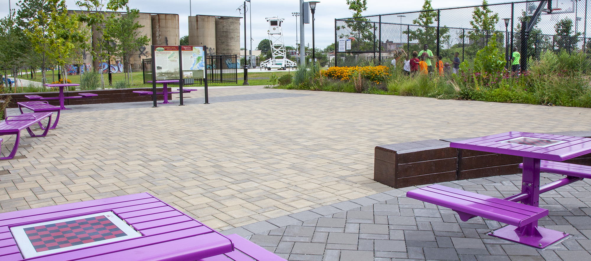 A parkette with different colors and shapes of Eco-Priora permeable pavers features bright picnic tables with checkerboards in them.