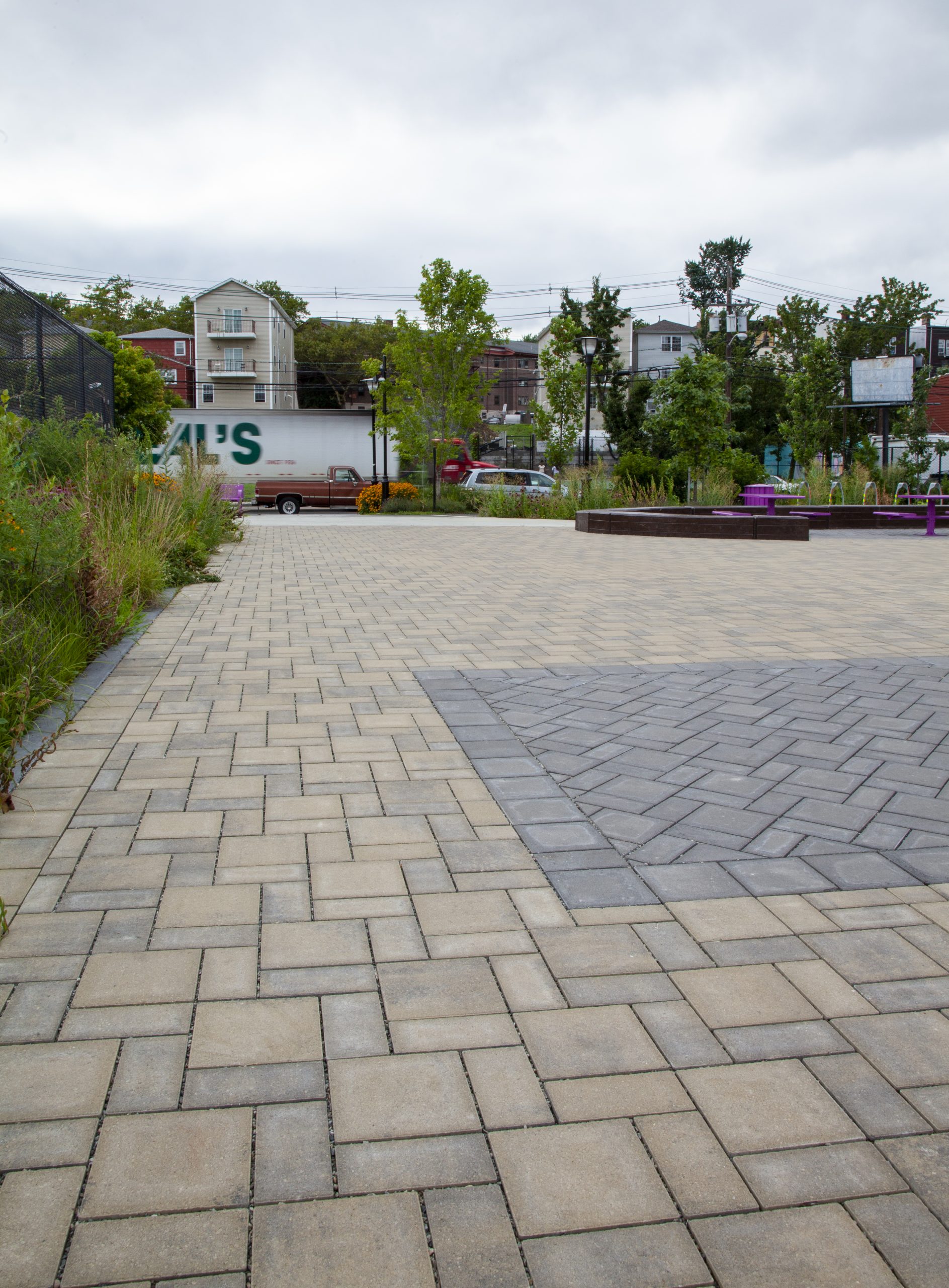 A parkette with different colors and shapes of Eco-Priora permeable pavers is surrounded by gardens and trees.