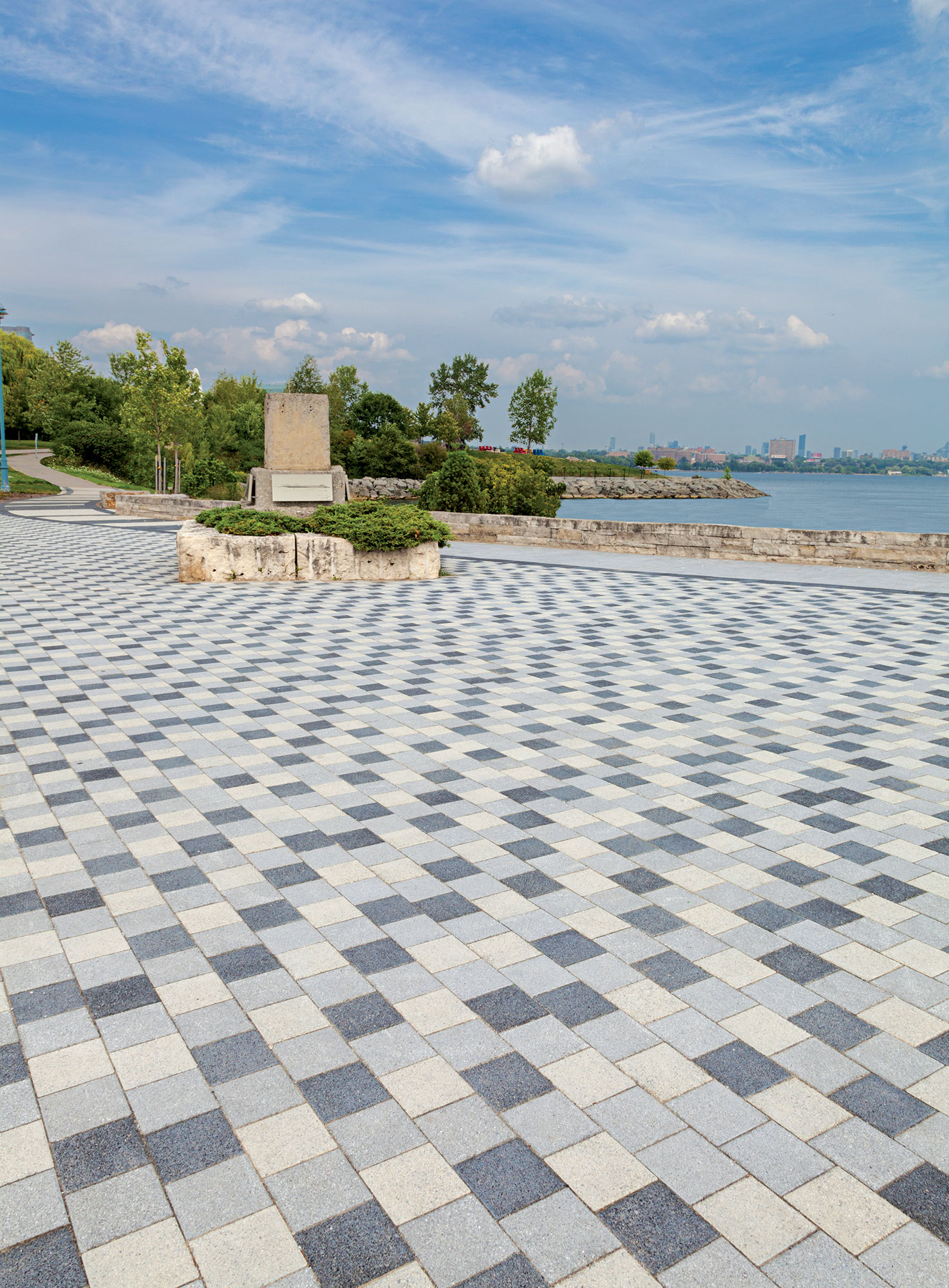Tri-colored Series pavers create a stunning checkerboard pattern near the shoreline, as a distinct garden island and sculpture sits nearby.